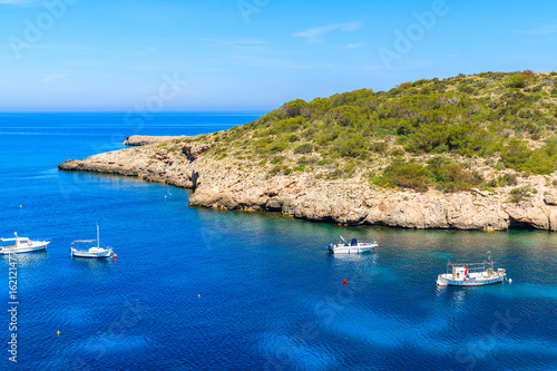 Motor and fishing boats on blue sea in Cala Portinatx bay, Ibiza island, Spain