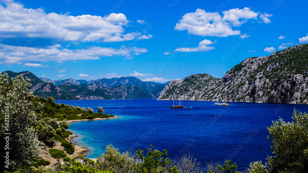 The landscape of blue sea with a boat, mountains and trees.