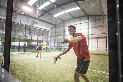 Defensive action in paddle tennis bouncing ball against glass. Man shot photo