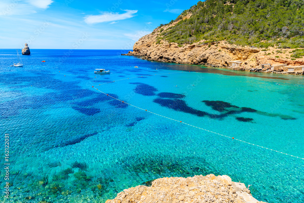 View of Cala Benirras bay with fishing boat on azure blue sea water, Ibiza island, Spain