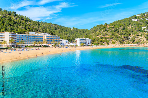 Azure sea water and hotel buildings on beach in Cala San Vicente bay, Ibiza island, Spain