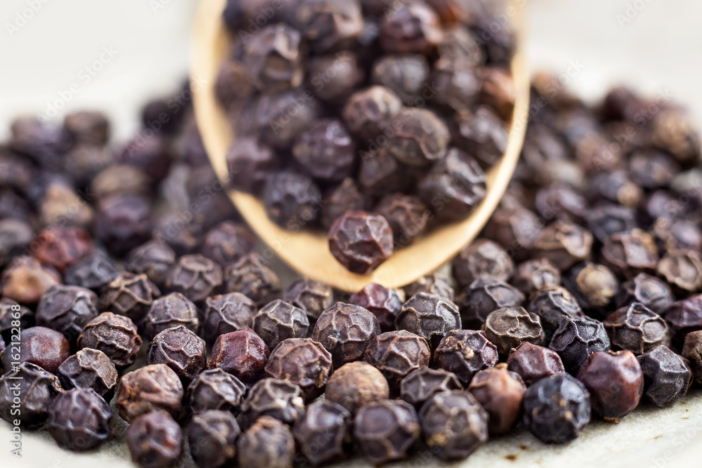 black peppercorns on wooden spoon. closeup dried seeds. black peppercorns on wooden spoon. closeup dried seeds.