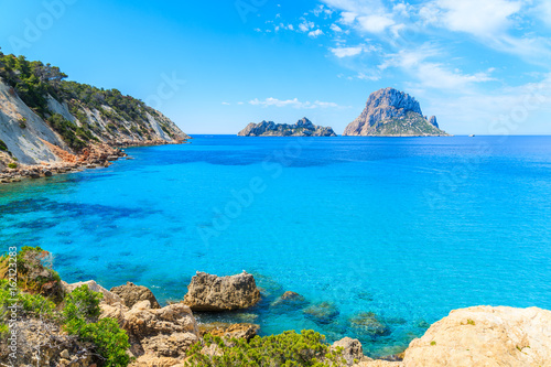 View of Cala d'Hort bay with beautiful azure blue sea water and Es Vedra island in distance, Ibiza island, Spain photo
