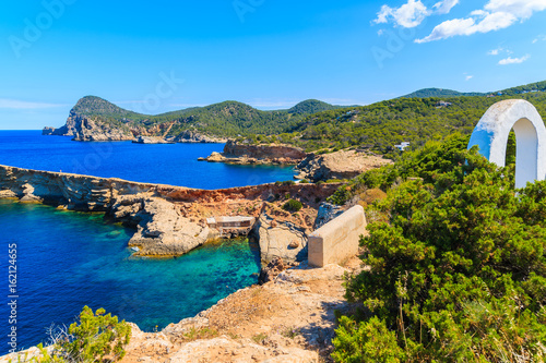 White arch gate on coastal path to Punta Galera bay surrounded by amazing stone formations, Ibiza island, Spain photo