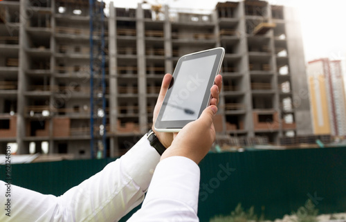 Closeup of young male hand holding digital tablet with building site on background