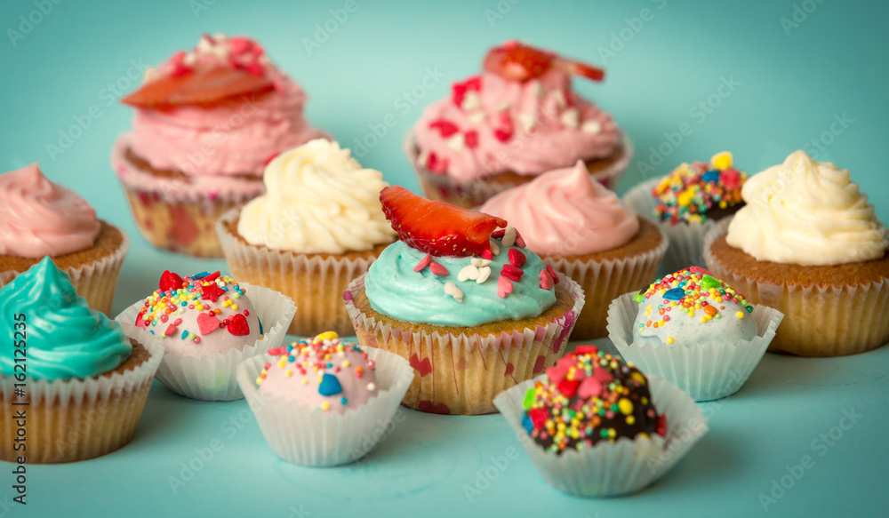 Tasty freshly baked cupcakes and colorful candies over turquoise background