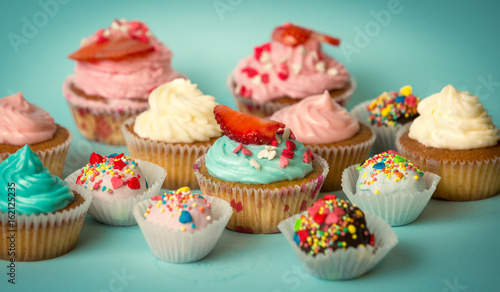 Tasty freshly baked cupcakes and colorful candies over turquoise background