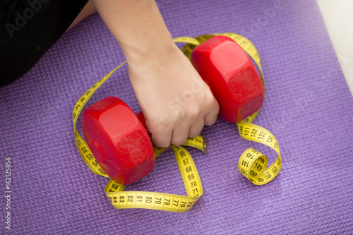 Closeup photo of hand lifting dumbbell covered by measuring tape