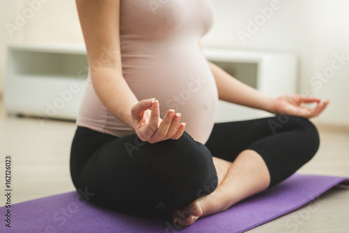 Closeup photo of pregnant woman sitting in yoga lotus position