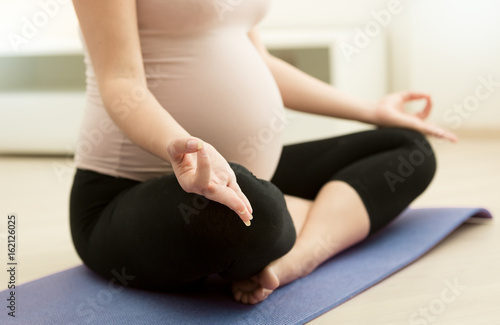 Closeup image of pregnant woman practicing yoga at home