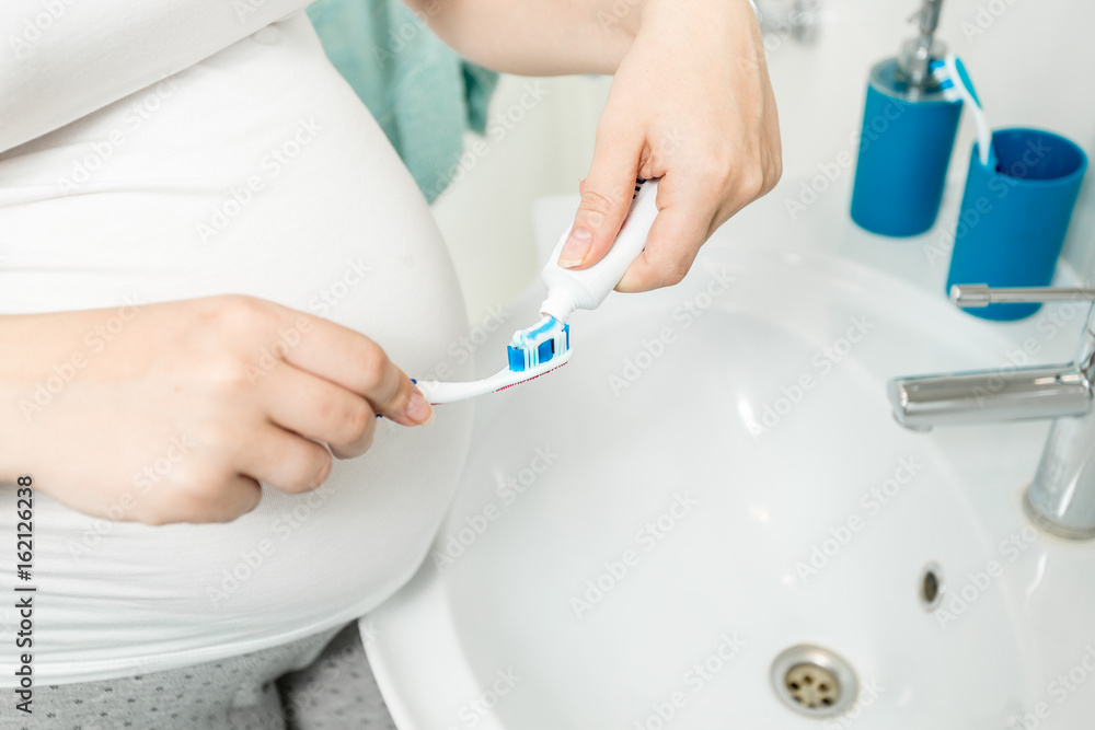 Closeup image of woman putting toothpaste on toothbrush at bathroom Closeup image of woman putting toothpaste on toothbrush at bathroom