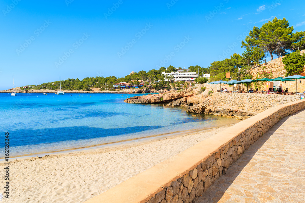 Coastal promenade along Cala Portinatx beach with azure blue sea water, Ibiza island, Spain