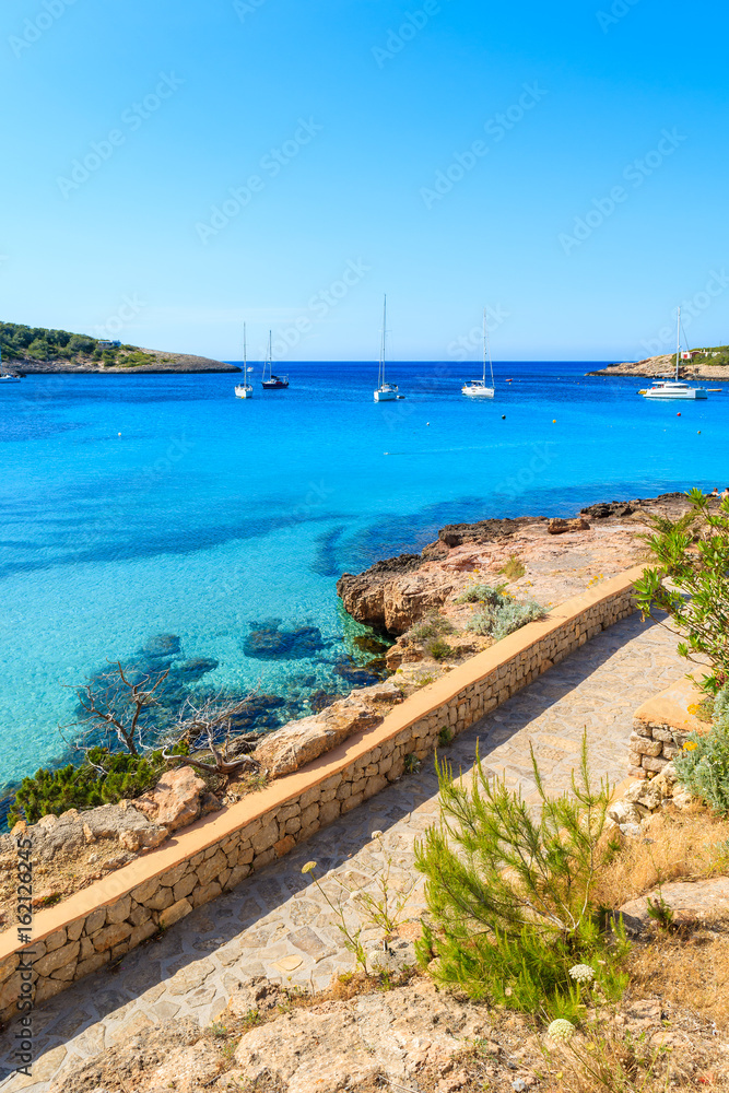 View of coastal promenade along blue sea in Cala Portinatx bay, Ibiza island, Spain