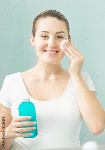 Portrait of beautiful smiling woman cleaning face with lotion