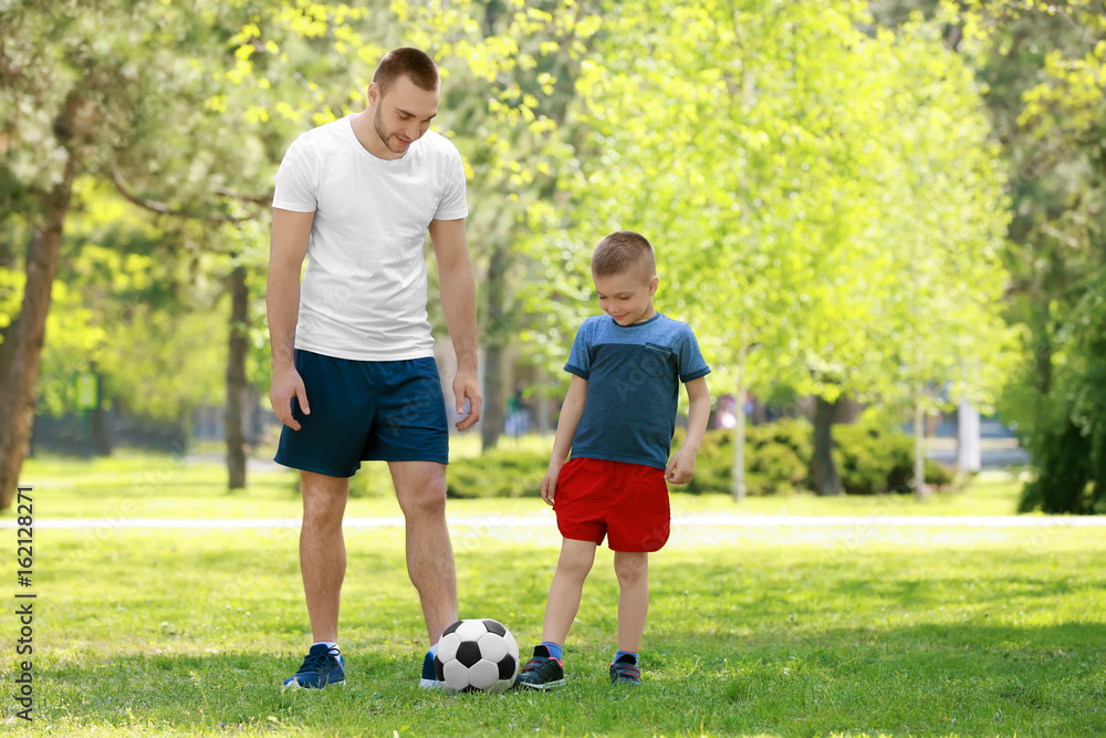 Father and son playing football on green grass in park Father and son playing football on green grass in park