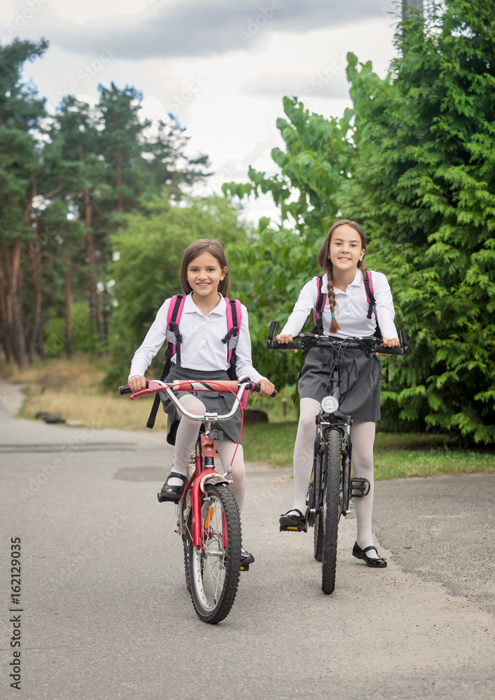 Two smiling girls riding bicycles to school