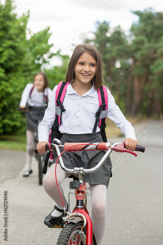 Happy smiling girl in school uniform riding bicycle