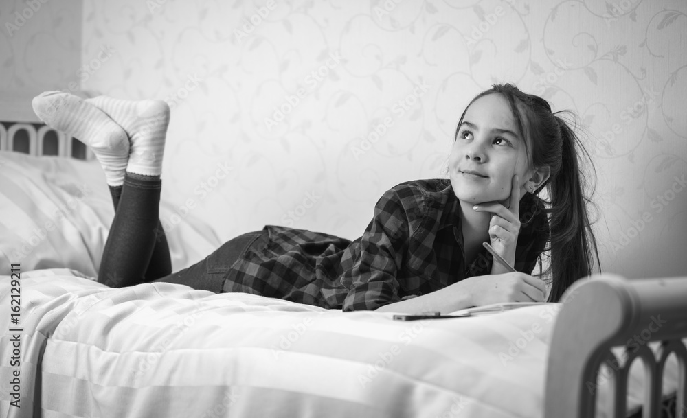 Black and white image of thoughtful teenage girl lying on bed at