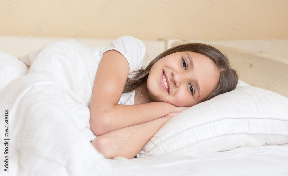 Cute smiling girl lying on pillow and looking at camera