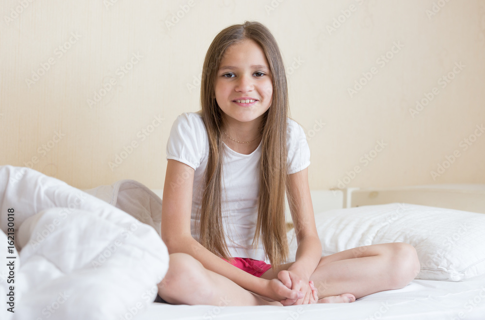 Smiling girl with long dark hair sitting on bed Smiling girl with long dark hair sitting on bed