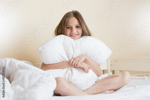 Beautiful brunette girl sitting on bed and hugging white pillow