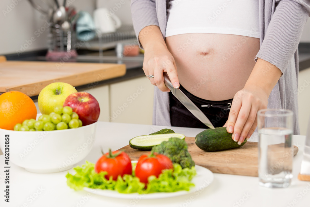 Closeup photo of pregnant woman making salad on kitchen