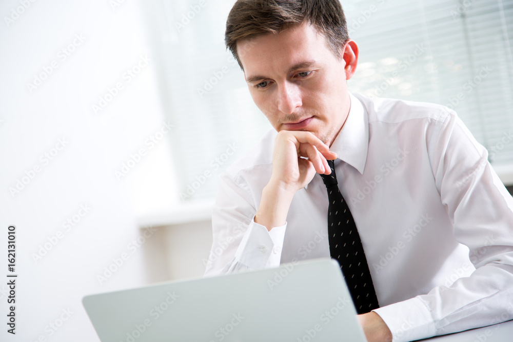 Handsome young businessman working at laptop in office. Handsome young businessman working at laptop in office.