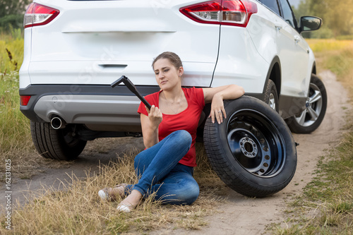 Young woman sitting next to broken car and trying to change flat tire © Кирилл Рыжов