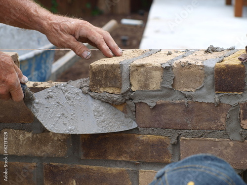Fotografie In a demonstration, a master brick mason demostrates the use of a trowel in brick and mortar work