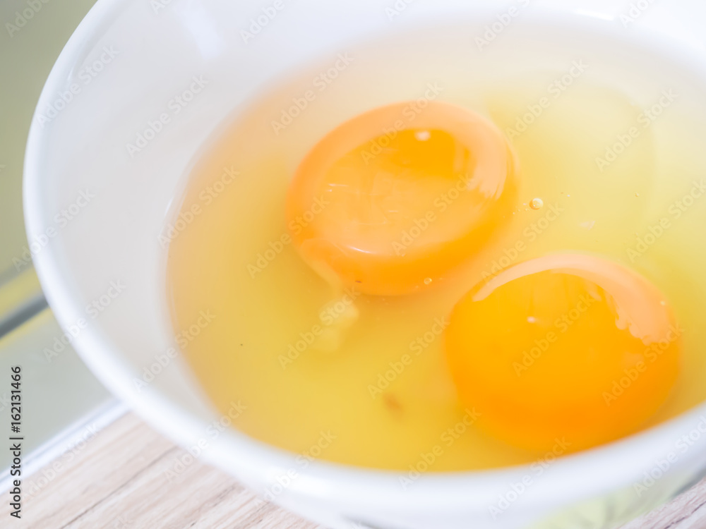 Closeup of two eggs yolk and egg white in white bowl for cooking Closeup of two eggs yolk and egg white in white bowl for cooking