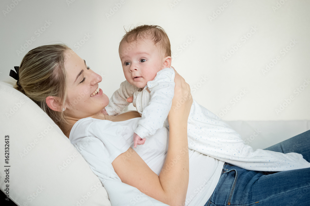 Portrait of cheerful young mother lying with her baby on bed