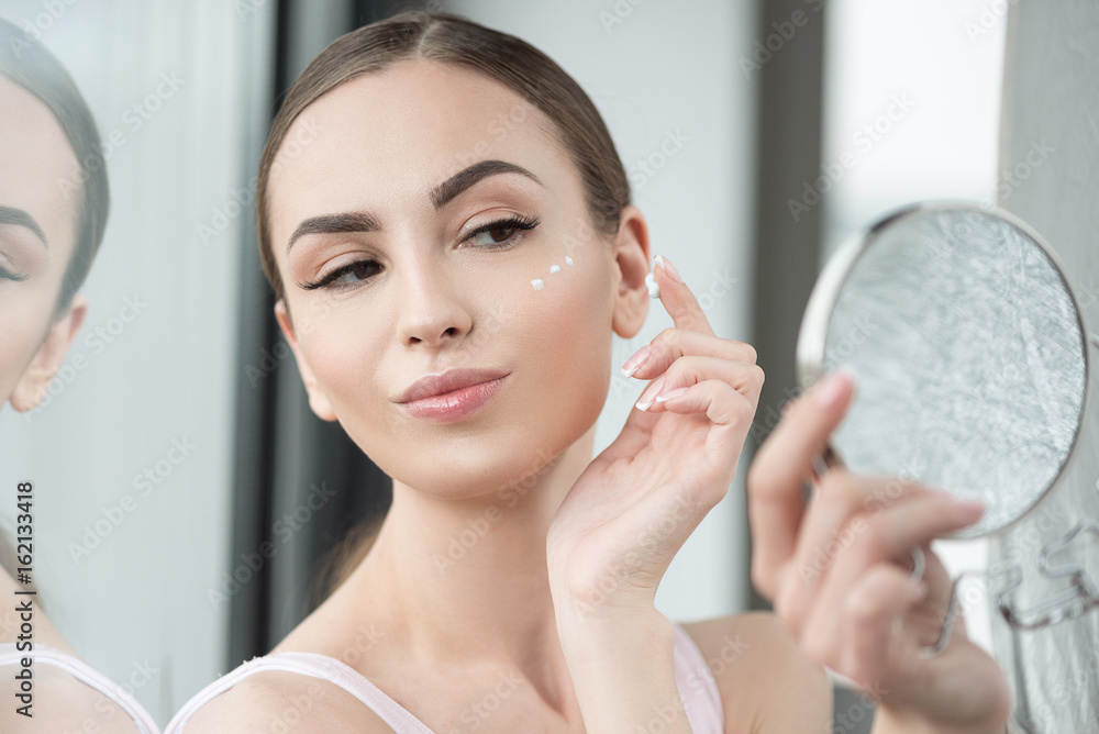 Happy youthful woman applying make-up on face skin