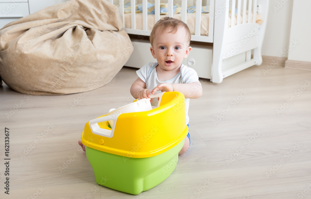 Baby boy playing with chamber pot on floor at living room Baby boy playing with chamber pot on floor at living room