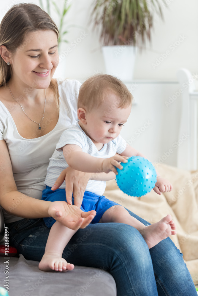 Beautiful young mother playing with her baby boy on sofa with ball Beautiful young mother playing with her baby boy on sofa with ball