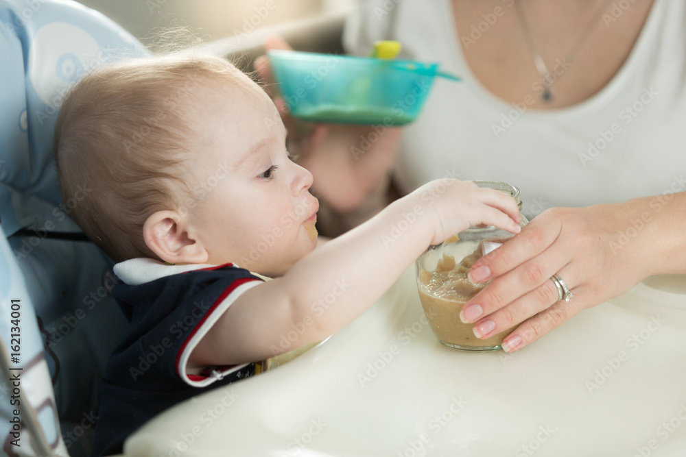 Woman feeding her baby from spoon with apple sauce - obrazy, fototapety, plakaty 