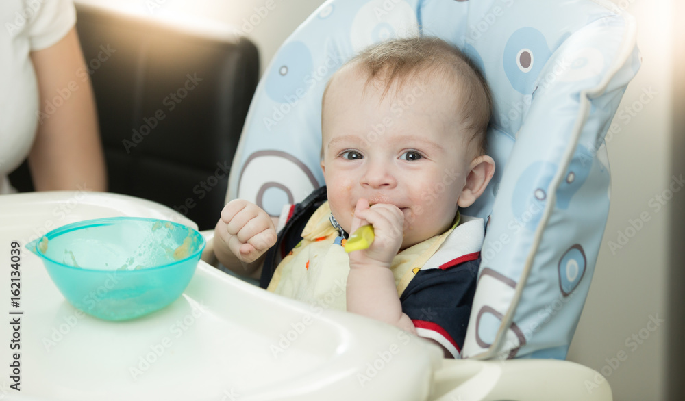 Closeup of baby sitting in highchair and holding spoon Closeup of baby sitting in highchair and holding spoon