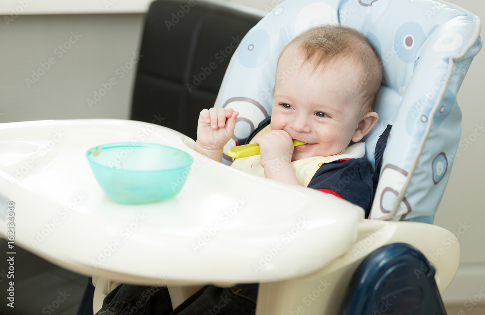 Baby boy sitting in highchair and playing with spoon and dish Baby boy sitting in highchair and playing with spoon and dish