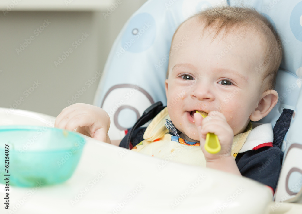 Adorable 9 months old boy eating in highchair at kitchen Adorable 9 months old boy eating in highchair at kitchen