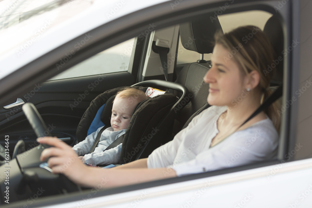 Young mother driving car with her baby boy sitting in car in baby seat