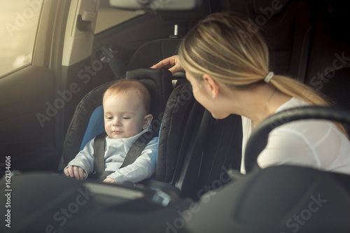 Smiling young mother looking at her child sitting in safety seat