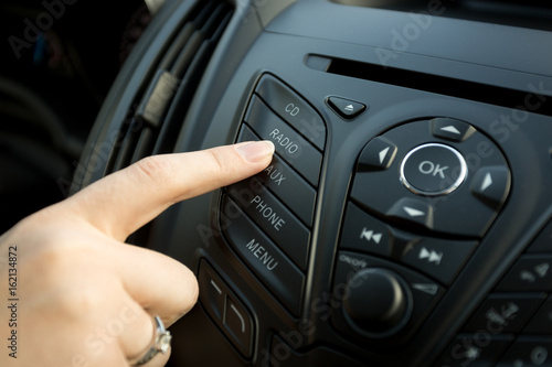 Closeup of female finger pressing radio button on car control panel