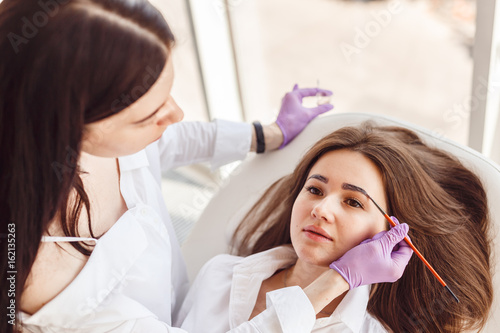 Top view of a woman a client lies on the procedure for eyebrow correction. Young women tweezing her eyebrows in beauty salon.