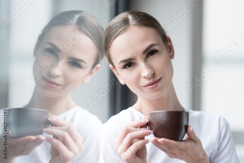 Happy attractive girl resting with hot drink indoors
