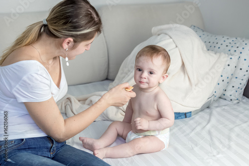 Parent giving biscuit for babies to 9 months old son at bedroom