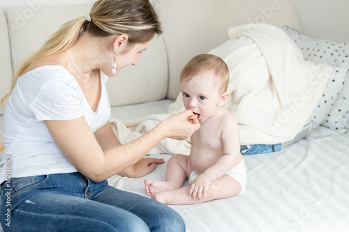 Billede på lærred Beautiful young mother sitting with her baby on sofa and giving him a cookie