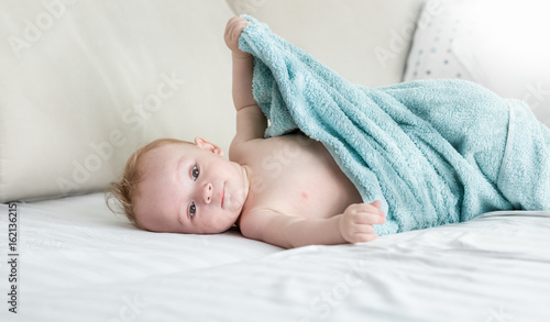 9 months old baby boy sitting on bed under towel
