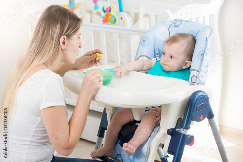 Mother feeding her baby in highchair at living room