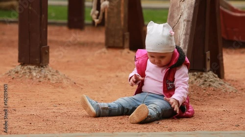 Cute little baby girl dressed in the pink clothing sitting on the playground in outdoor.