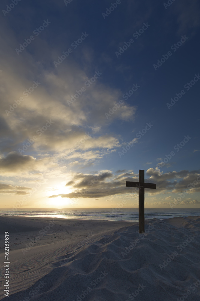 An old cross on sand dune next to the ocean with a calm sunrise