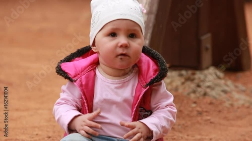 Cute little baby girl dressed in the pink clothing sitting on the playground in outdoor.